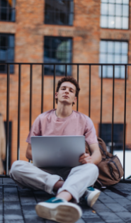 Person sitting with a laptop near brick building